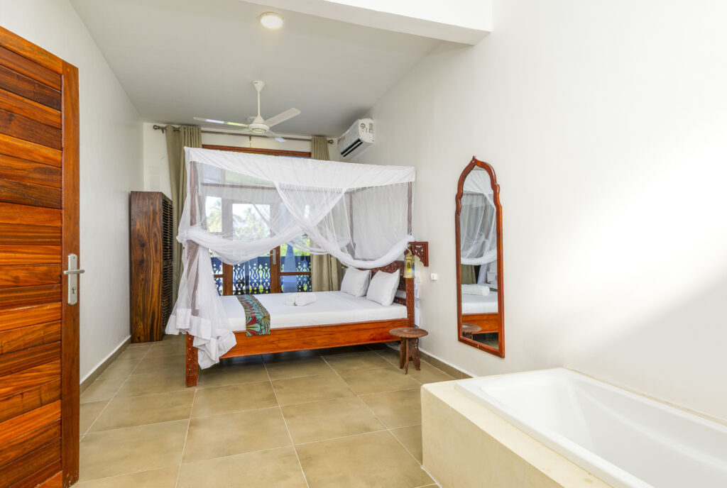 Elegant bedroom featuring a bed, wall-mounted mirror, and attached bathroom with a bathtub at Tasneem Hotel Zanzibar